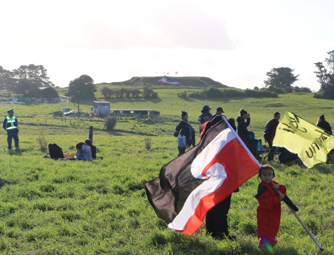 A+young+girl+with+her+mother+holds+aloft+Tino+Rangatiratanga+%E2%80%93+the+M%C4%81ori+flag+of+independence+at+Ihum%C4%81tao.+Image%3A+Michael+Andrew%2FPMC